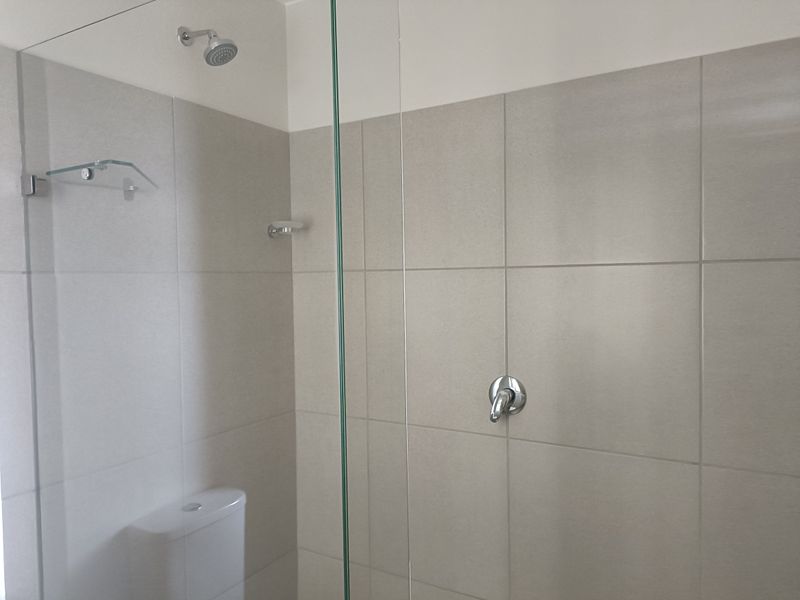 A clean, modern bathroom featuring a glass-enclosed shower with neutral ceramic wall tiling and a standard toilet.
