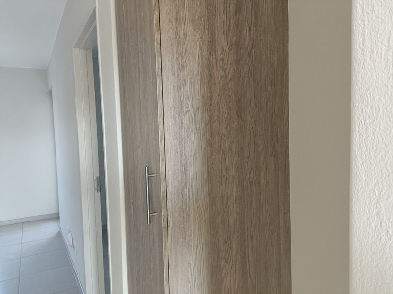 A clean, neutral hallway featuring light-toned wood-look built-in cabinetry and tiled flooring, leading to an adjacent room.