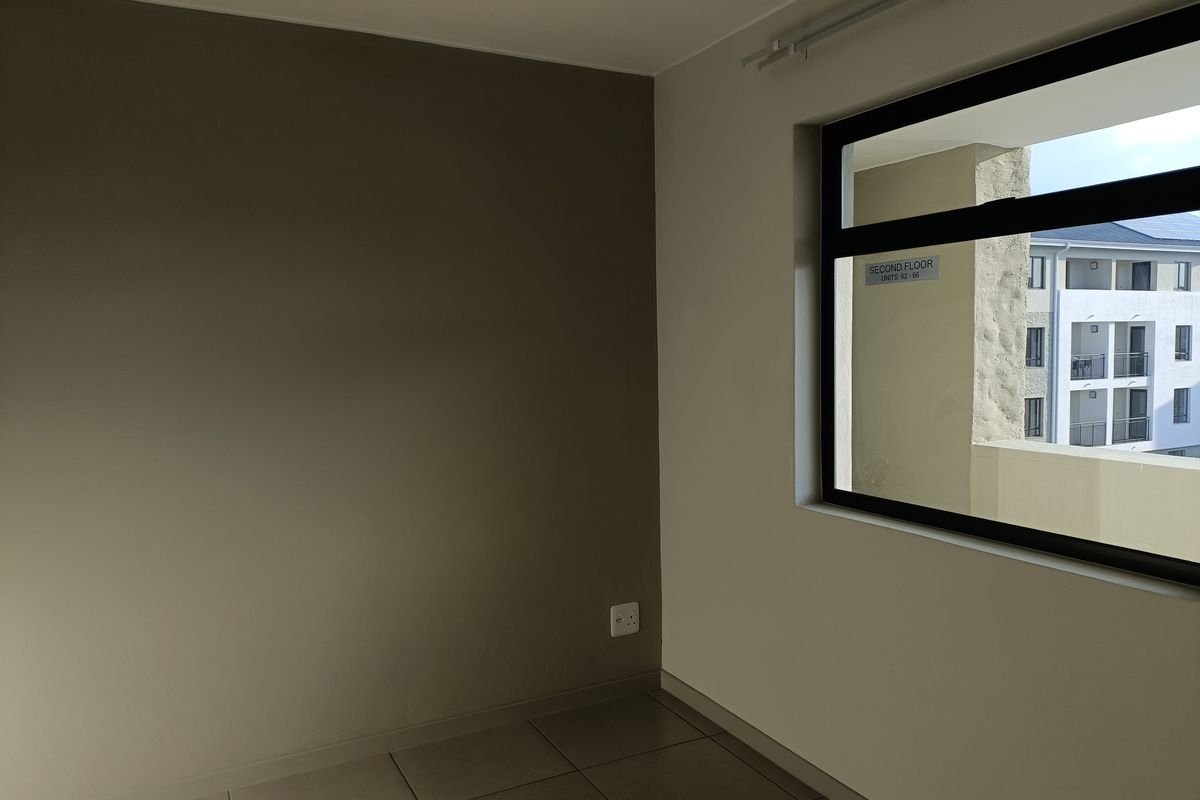 A clean, empty bedroom featuring neutral-toned walls, tiled flooring, and a large window with an exterior view of the apartment complex.