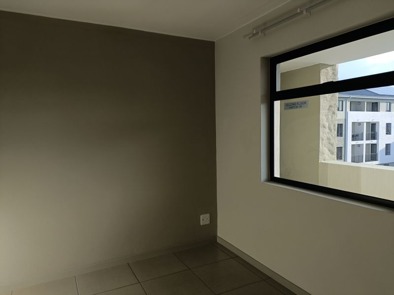 A clean, empty bedroom featuring neutral-toned walls, tiled flooring, and a large window with an exterior view of the apartment complex.