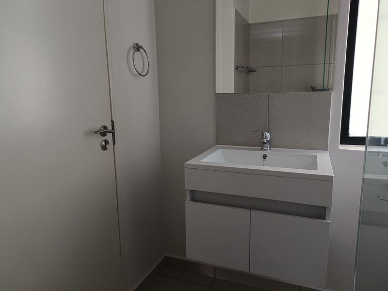 A clean, modern bathroom featuring a wall-mounted vanity with a basin, mixer tap, and a large mirror with tiled splashback.