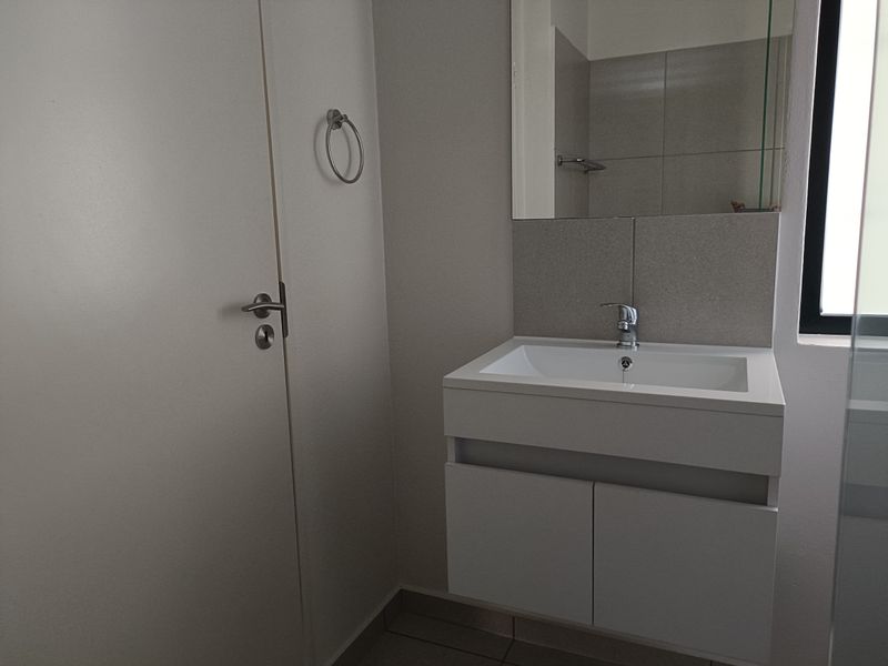 A clean, modern bathroom featuring a wall-mounted vanity with a basin, mixer tap, and a large mirror with tiled splashback.