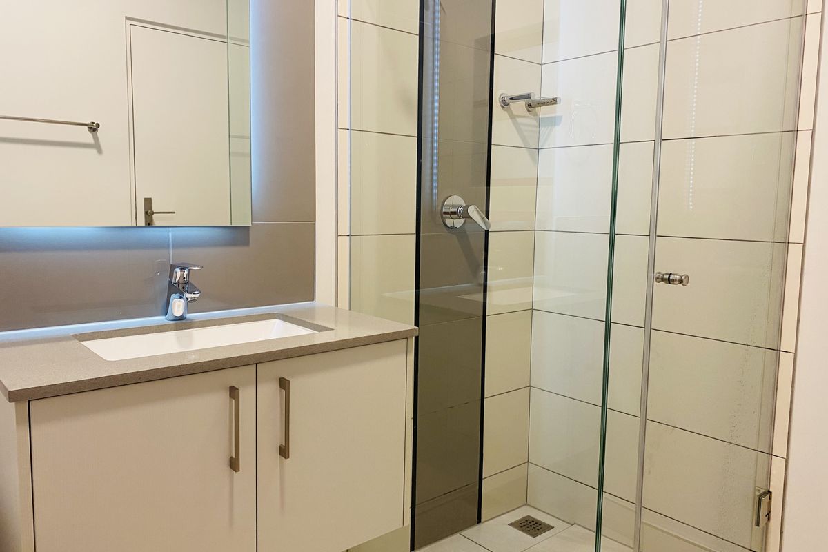 Modern bathroom featuring a floating vanity with stone countertop, undermount basin, and a spacious glass-enclosed shower with contemporary fixtures.
