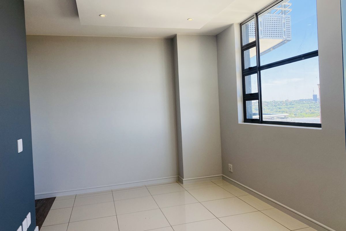 A bright, empty living area featuring modern tiled flooring, recessed ceiling lighting, and a large window offering expansive views.