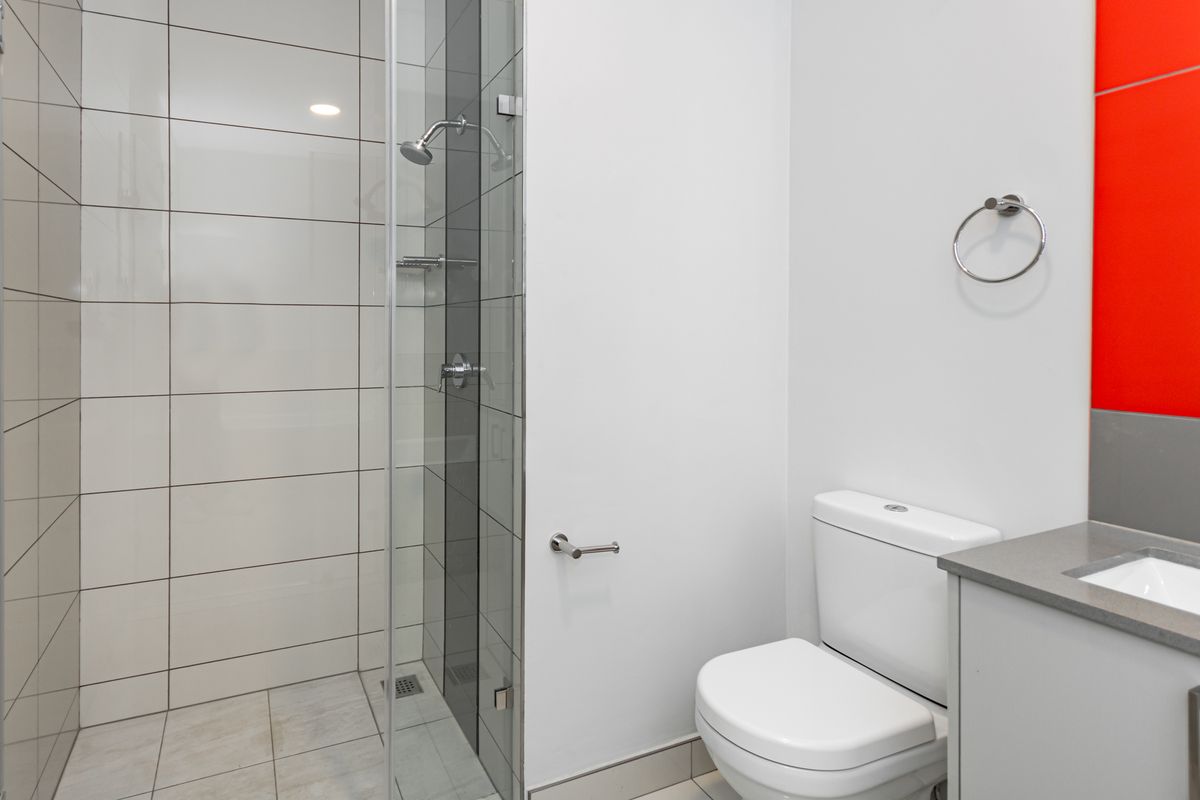 Modern bathroom featuring a glass-enclosed shower, white wall tiling, a sleek vanity with basin, and a standard toilet.