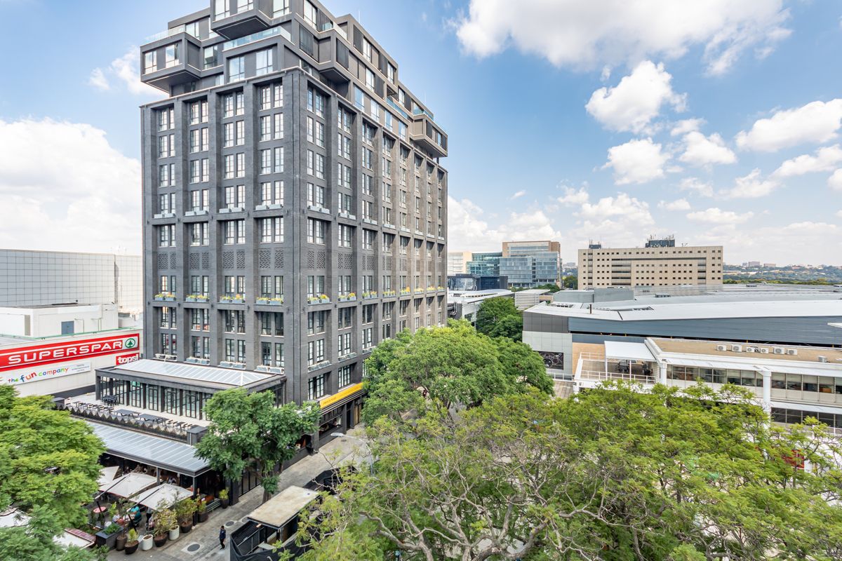An elevated aerial view of a modern high-rise apartment building situated in a vibrant urban environment with surrounding commercial infrastructure.