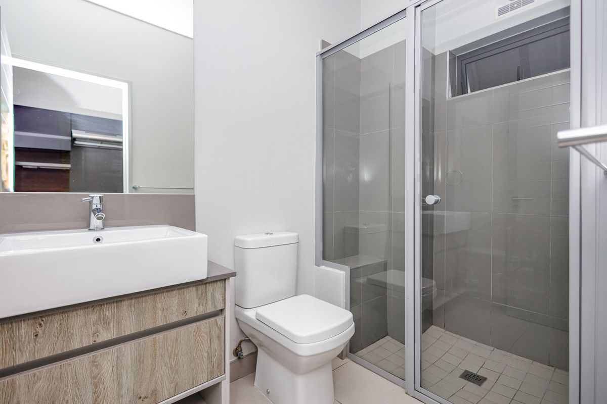 Modern bathroom featuring a wood-finish vanity with a vessel sink, a backlit mirror, a toilet, and a glass-enclosed shower with tiled finishes.