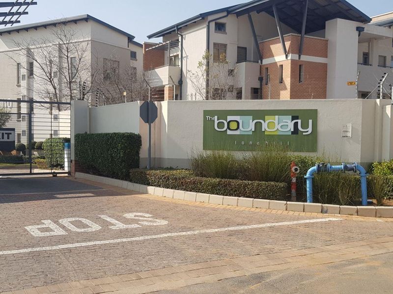 The entrance to The Boundary complex, featuring a secure gated access point, paved driveway, and perimeter wall with integrated signage.