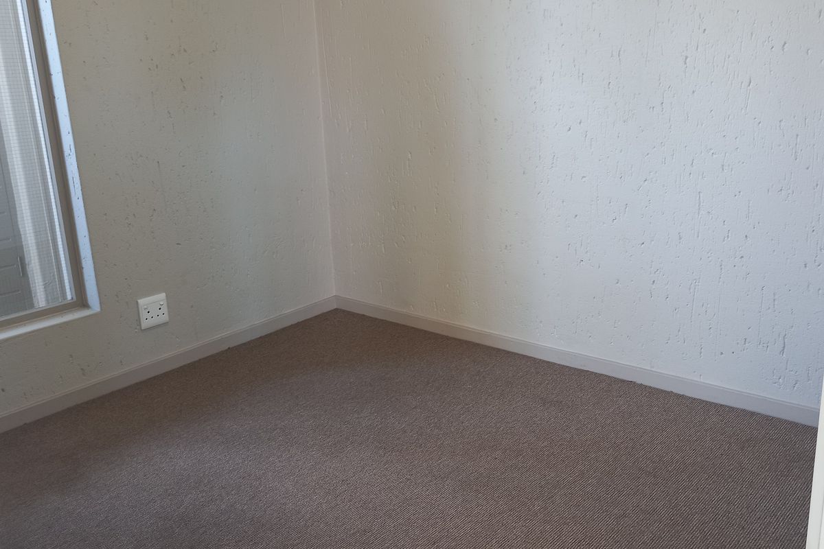 An empty bedroom featuring neutral carpet flooring and textured walls, providing a blank canvas for personalization.