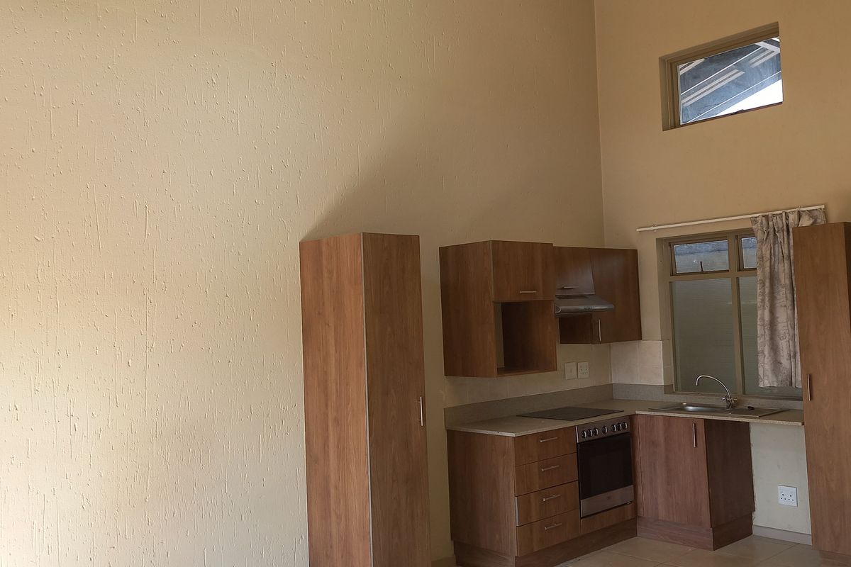 A compact kitchen featuring wood-finish cabinetry, built-in oven and hob, stainless steel sink, and tiled flooring under a high vaulted ceiling.