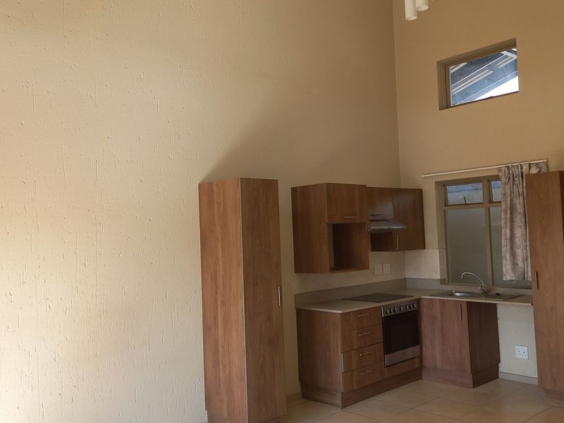 A compact kitchen featuring wood-finish cabinetry, built-in oven and hob, stainless steel sink, and tiled flooring under a high vaulted ceiling.