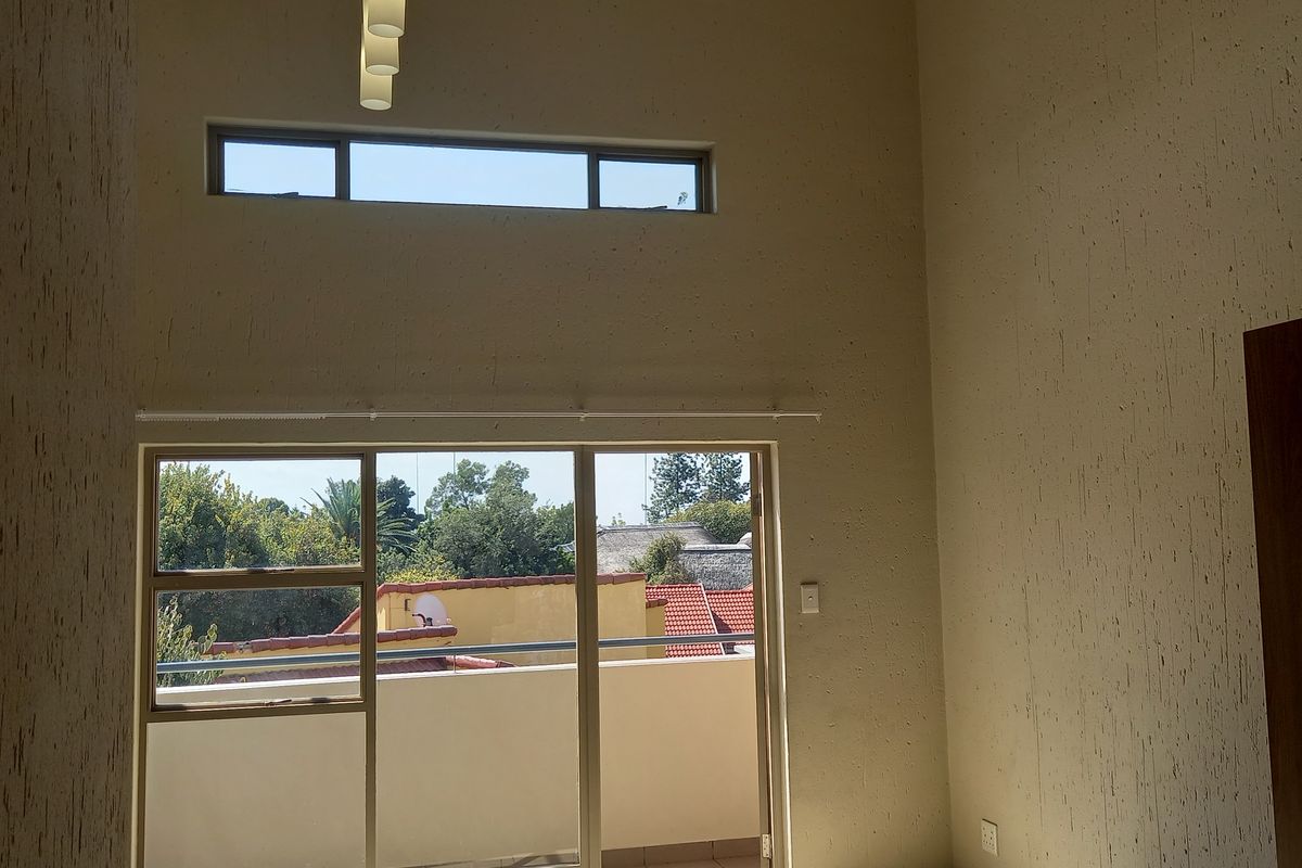 Spacious living area featuring high vaulted ceilings, tiled floors, and large sliding glass doors opening onto a private balcony with natural light.