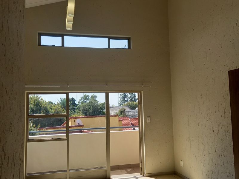 Spacious living area featuring high vaulted ceilings, tiled floors, and large sliding glass doors opening onto a private balcony with natural light.
