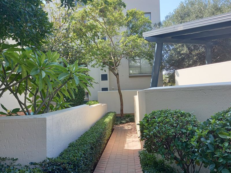 A well-maintained rear exterior area featuring a brick paved pathway, landscaped hedging, and a covered patio structure.