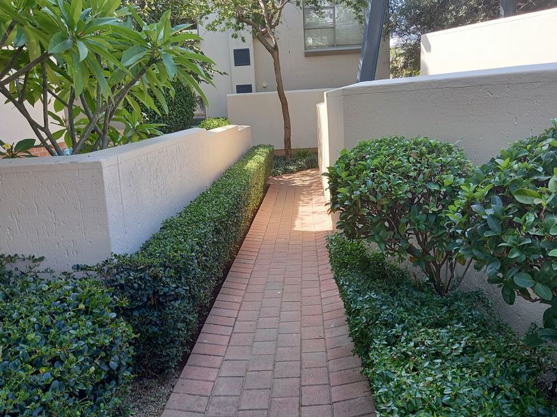 A well-maintained brick paved walkway leading through a landscaped garden area with neat hedges and retaining walls.