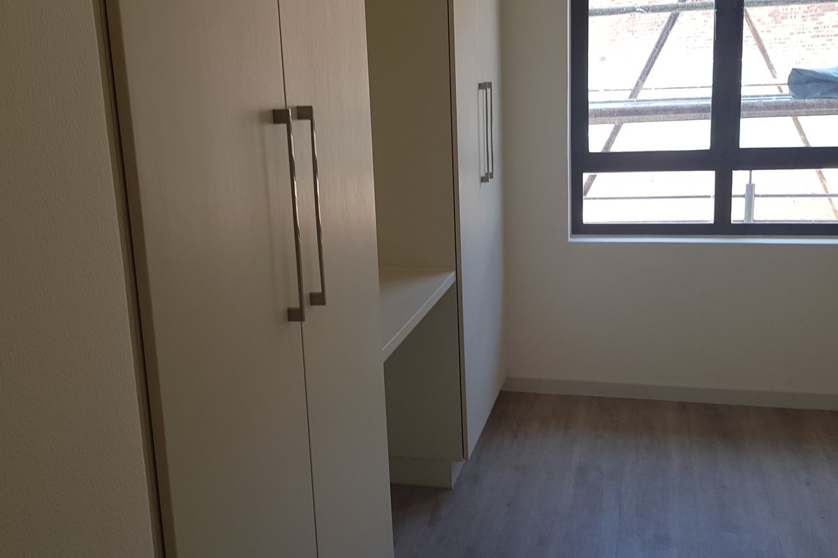 A bright, empty bedroom featuring modern laminate flooring and built-in cupboards with sleek handles.