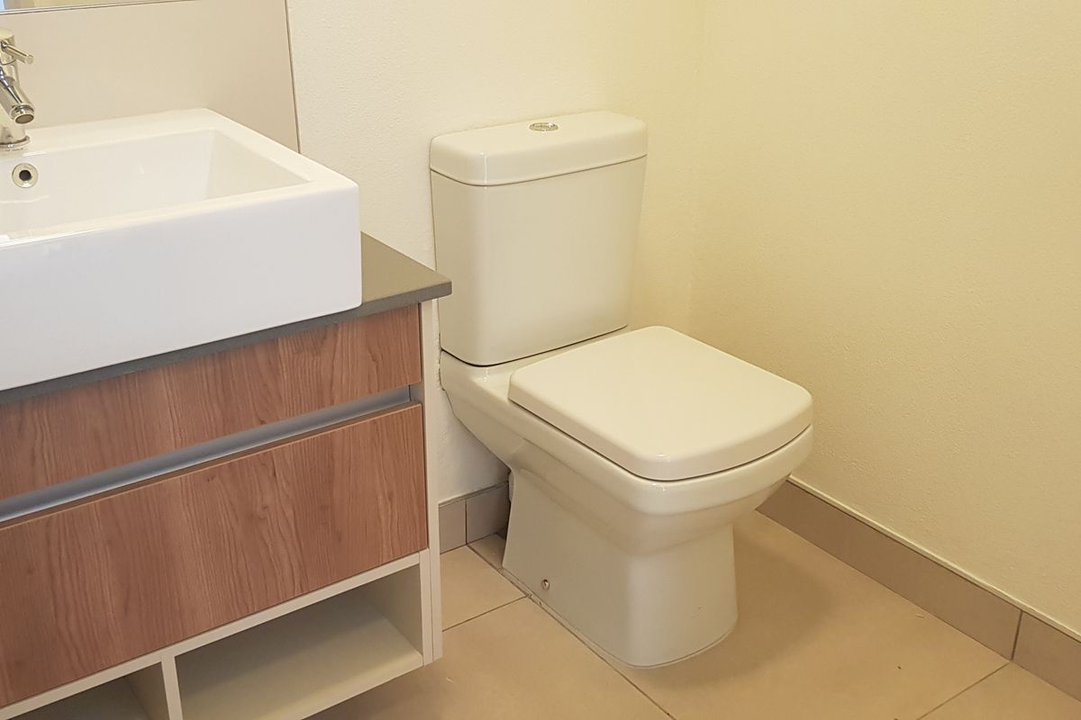 A clean, modern bathroom featuring a wood-finish vanity with a white ceramic basin, chrome tapware, and a standard toilet.