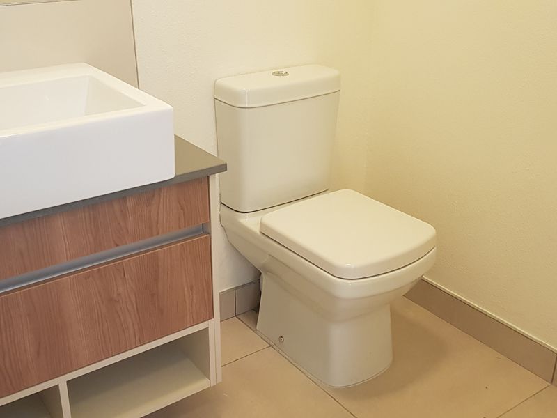 A clean, modern bathroom featuring a wood-finish vanity with a white ceramic basin, chrome tapware, and a standard toilet.