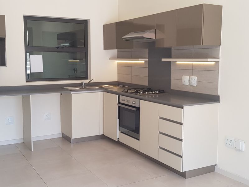 Modern, empty kitchen featuring sleek two-tone cabinetry, stone countertops, integrated gas hob, oven, and extractor fan with neutral tiled flooring.
