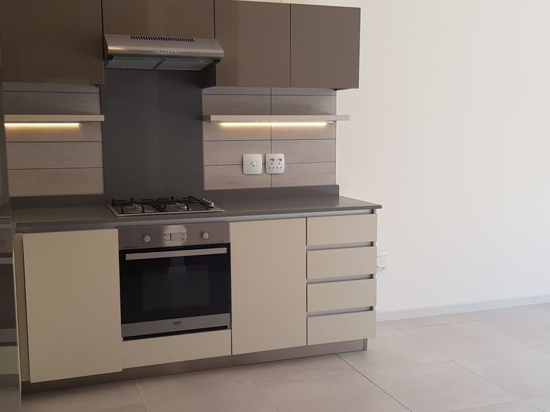 A modern, compact kitchen featuring sleek cabinetry, a built-in oven, gas hob, extractor fan, and neutral tiled flooring in an open-plan layout.