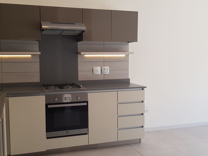 Modern kitchen featuring sleek two-tone cabinetry, built-in gas hob, electric oven, extractor fan, and integrated under-cabinet lighting in a clean, minimalist space.