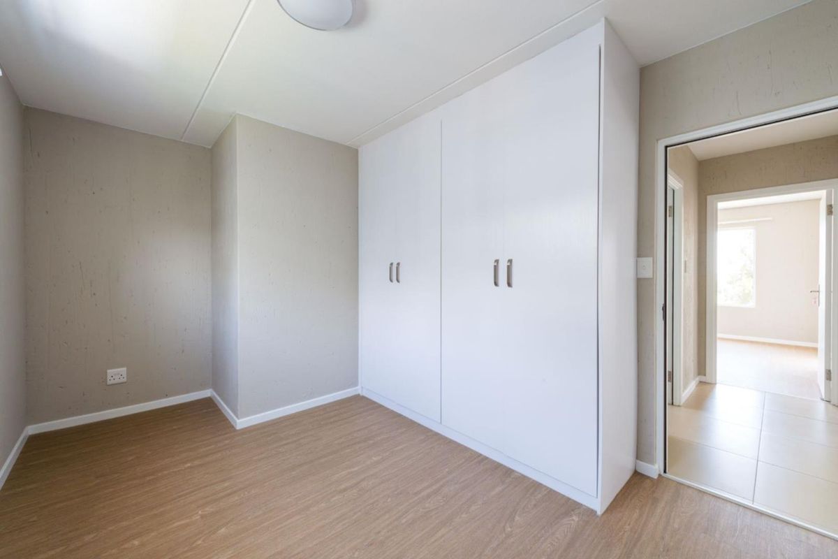 A clean, empty bedroom featuring neutral walls, laminate flooring, and ample built-in cupboard storage space.