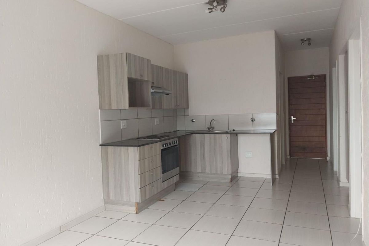 A clean, empty kitchen featuring modern wood-look cabinetry, built-in oven and hob, tiled backsplash, and neutral floor tiles in an open-plan layout.