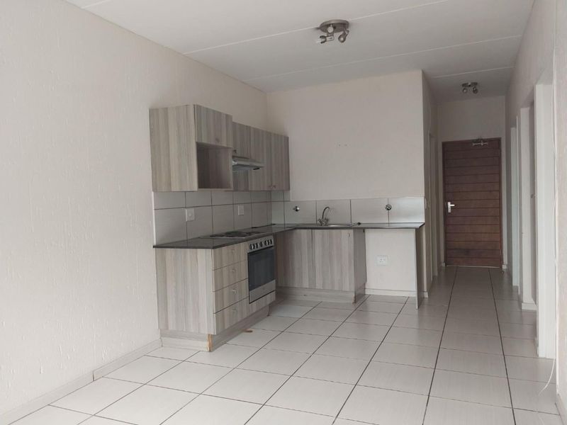 A clean, empty kitchen featuring modern wood-look cabinetry, built-in oven and hob, tiled backsplash, and neutral floor tiles in an open-plan layout.