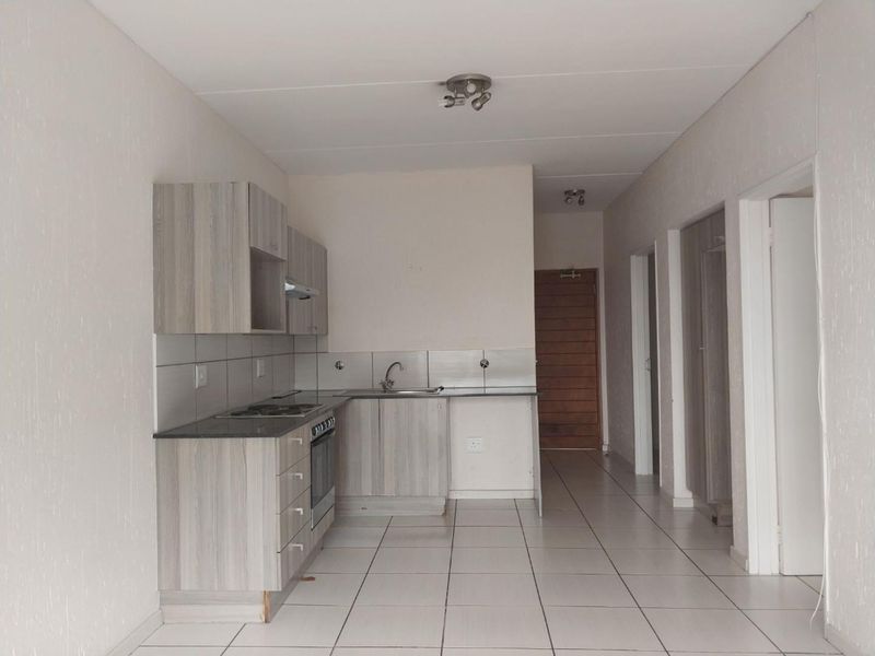 An empty kitchen featuring light wood-grain cabinetry, dark laminate countertops, a built-in oven with hob, and neutral tiled flooring throughout.