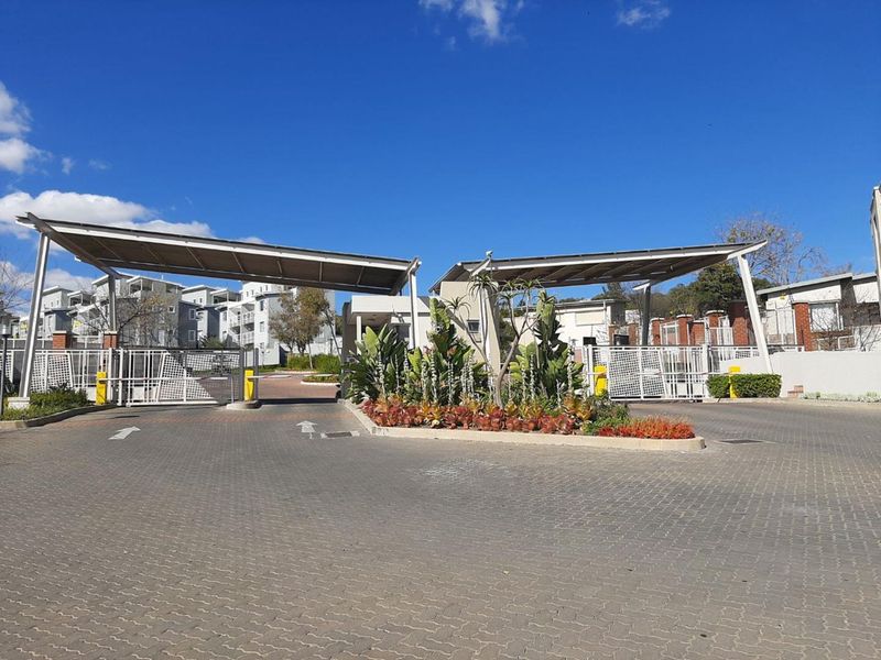 The main entrance to the apartment complex featuring a secure boom gate system, paved driveway, and solar panel covered access points.