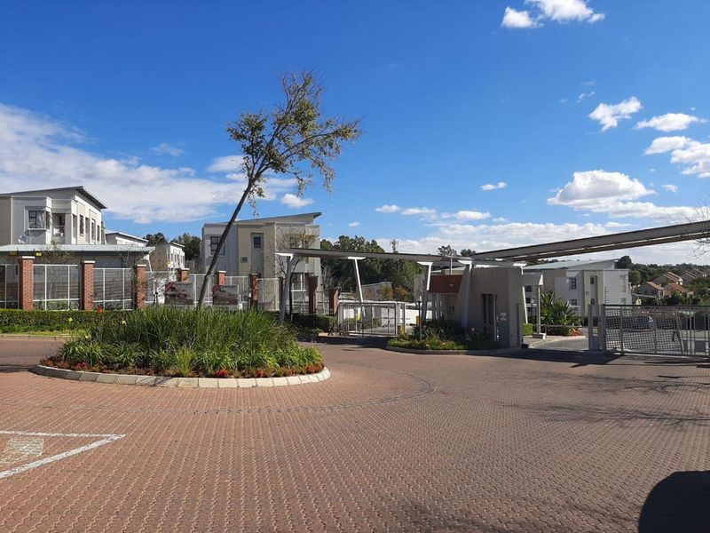 The entrance to the apartment complex features a secure gated access point, paved driveway, and well-maintained landscaped areas.