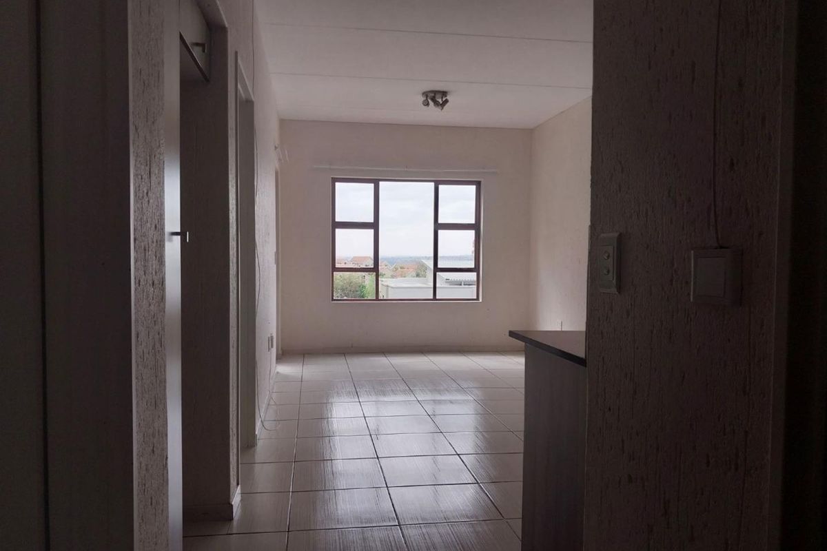 An empty, open-plan living area featuring neutral tiled flooring, a large window with natural light, and a built-in counter space.