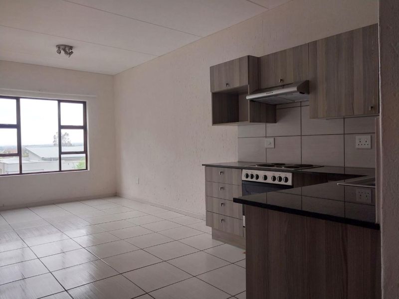An open-plan living and kitchen area featuring modern wood-finish cabinetry, granite countertops, a built-in stove, and neutral tiled flooring throughout.