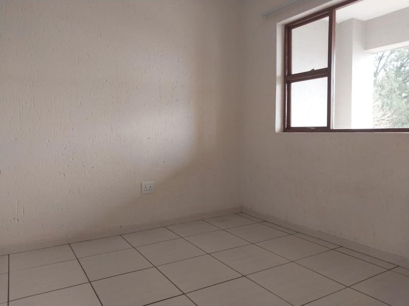 An empty bedroom featuring neutral tiled flooring, textured walls, and a brown aluminium window frame providing natural light.