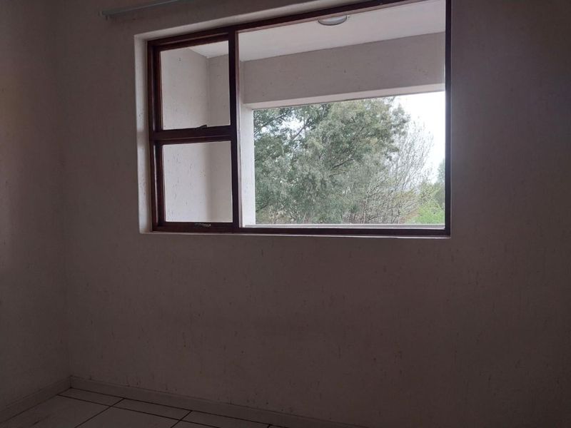 An empty bedroom featuring tiled flooring and a wooden window frame with views of surrounding trees.