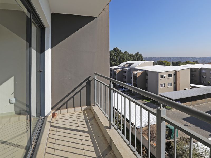 A clean, modern balcony featuring tiled flooring and a metal balustrade, offering an elevated view of the surrounding apartment complex and parking area.
