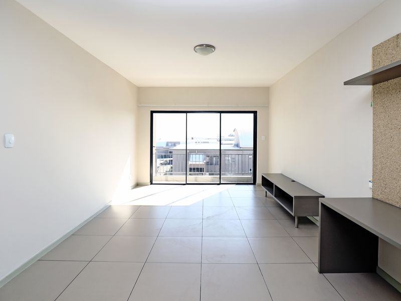 A bright, open-plan living area featuring large sliding glass doors, neutral tiled flooring, and built-in desk and shelving units.