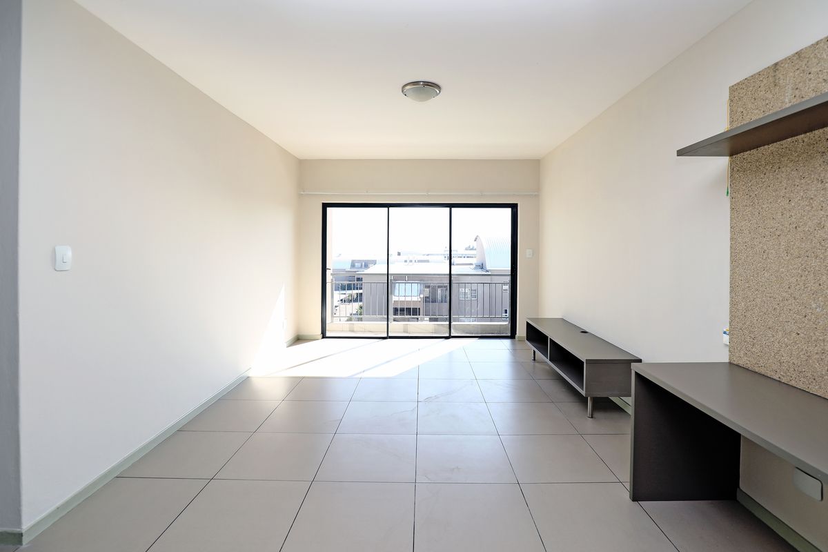 A bright, open-plan living area featuring large sliding glass doors, neutral tiled flooring, and built-in desk and shelving units.