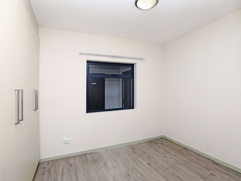 A clean, empty bedroom featuring modern laminate flooring, built-in cupboards, and a dark-framed aluminium window, providing a neutral canvas for personalization.