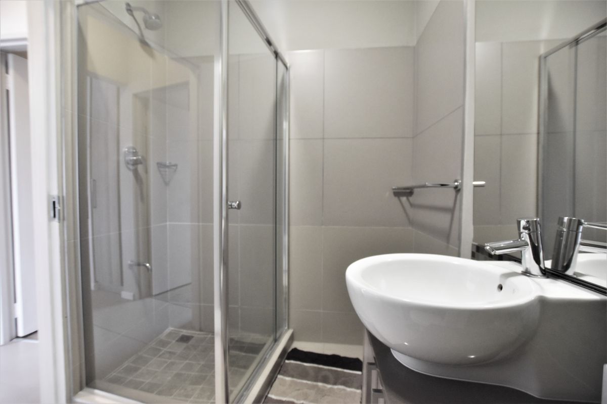 A modern bathroom featuring a glass-enclosed shower, neutral wall tiling, and a contemporary vessel sink with a chrome mixer tap.