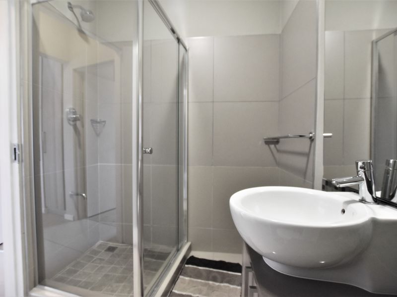A modern bathroom featuring a glass-enclosed shower, neutral wall tiling, and a contemporary vessel sink with a chrome mixer tap.