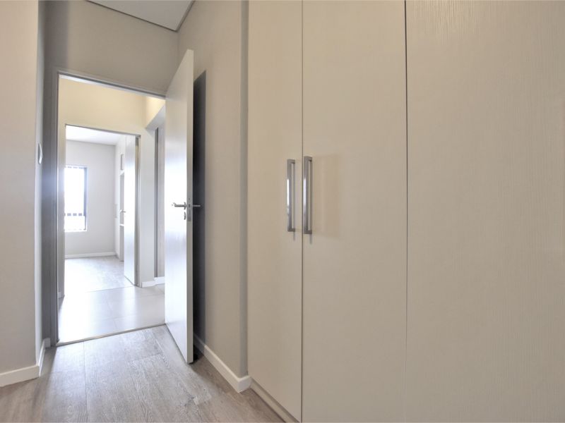 A clean, modern hallway featuring neutral walls, light laminate flooring, and ample built-in cupboard storage space.