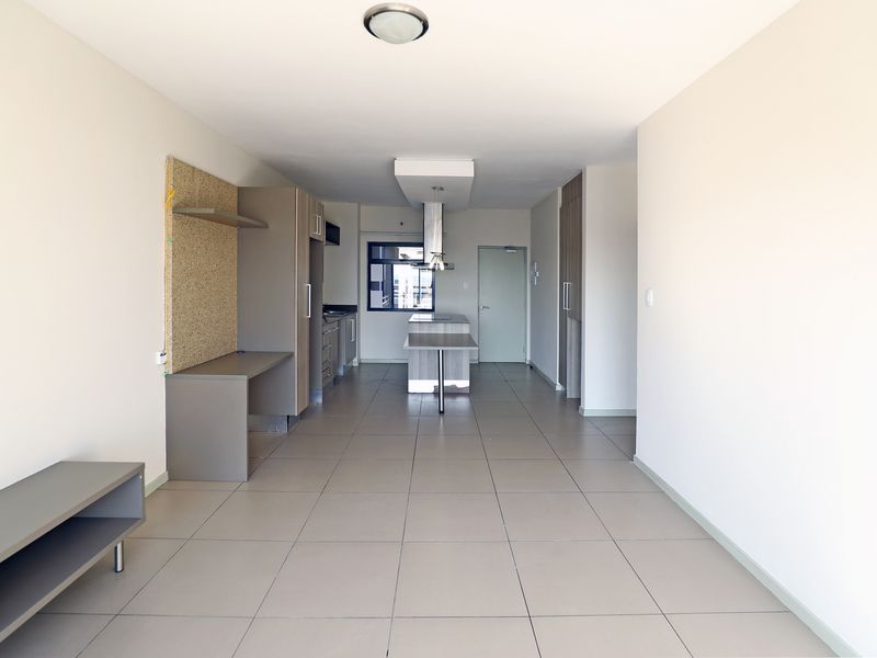 Spacious open-plan living and kitchen area featuring neutral tiled flooring, modern built-in cabinetry, a central kitchen island, and a dedicated built-in desk space.