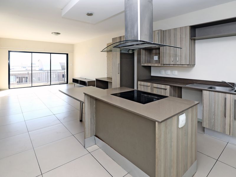 Modern open-plan kitchen and living area featuring a central island with hob, sleek cabinetry, tiled floors, and access to a balcony through sliding doors.