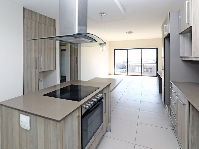 Modern open-plan kitchen featuring sleek cabinetry, stone countertops, and integrated appliances, flowing into a bright living area with large sliding doors.
