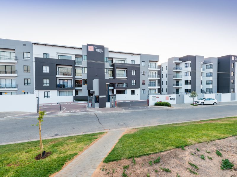 Modern apartment complex facade featuring contemporary grey and white architecture, secure gated entrance, and private balconies.