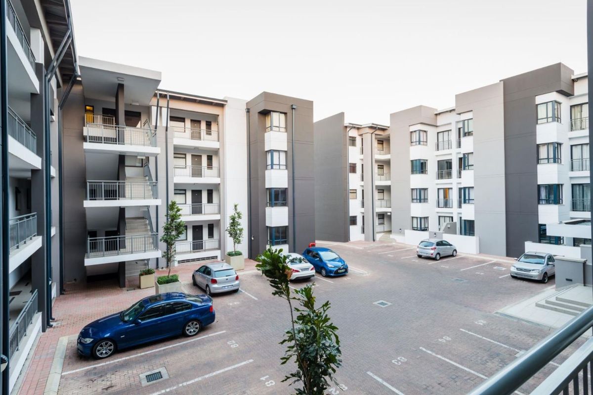 A view of the apartment complex courtyard featuring paved parking bays and multi-story residential blocks with external staircases and balconies.