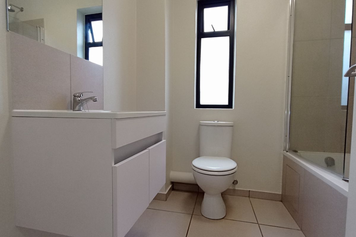 A clean and modern bathroom featuring a white vanity, toilet, and a bathtub with a glass shower screen.