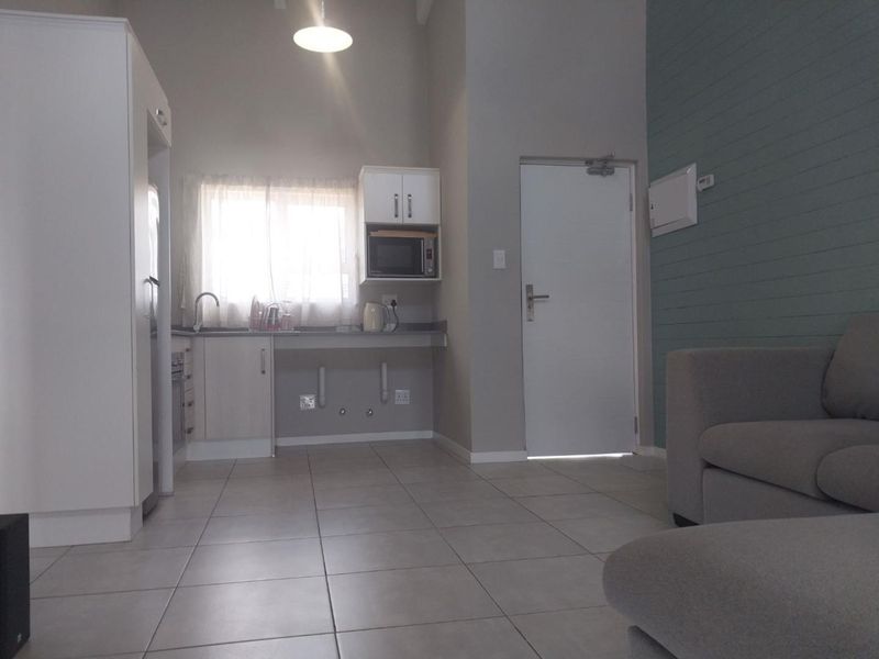 Open-plan living area featuring tiled floors, a compact kitchen with built-in cabinetry, and a decorative panelled feature wall.