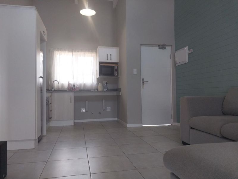 An open-plan living and kitchen area featuring neutral tiled flooring, built-in cabinetry, and a modern accent wall, providing a functional and bright living space.
